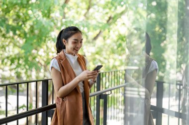 Genç bir kadın, sakin bir şehir ortamında balkonda akıllı telefonuyla iletişim kurmaktan hoşlanıyor..