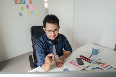 Renk paletleri ve tasarım araçları ile çevrili çağdaş bir stüdyo ortamında yetenekli grafik tasarımcısı, yaratıcı iş odaklı.