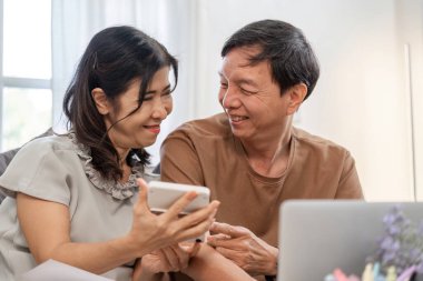 Yaşlı bir çift, hesap makinesi ve belge kullanarak aile gelirlerini ve giderlerini hesaplamak için bir masada birlikte otururlar..