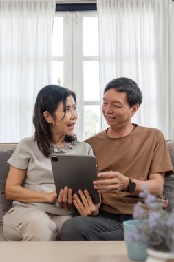 Emekli bir çift oturma odasında dinleniyor, modern dekorasyon ve doğal ışıkla çevrili rahat ve huzurlu bir yaşam tarzının tadını çıkarıyor..