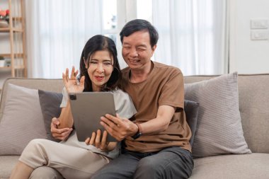 Emekli bir çift, çocuklarıyla bir tablet kullanarak, oturma odasındaki bir kanepede rahatça oturarak görüntülü sohbet ediyor..