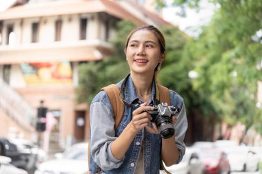 Kameralı neşeli bir kadın şehri keşfederken gülümsüyor, anları yakalıyor ve fotoğraf yolculuğunun tadını çıkarıyor..