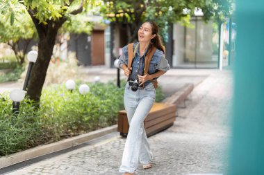 Genç bir kadın canlı bir şehir bölgesinde mutlu bir şekilde yürüyor, kamerasıyla anları yakalıyor. Macera ve yaratıcılık kavramı.