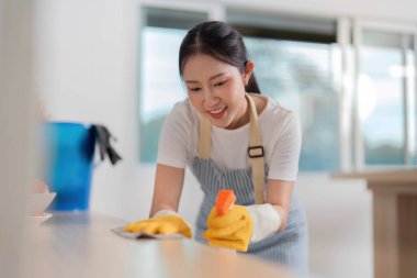 Neşeli bir kadın mutfak yüzeyini silip süpürüyor, temizlik rutinini coşkuyla yaparken gülümsüyor..