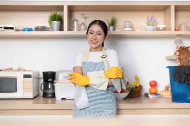 Önlüklü ve eldivenli gülümseyen bir kadın düzenli mutfağında duruyor, temizliğe hazır..