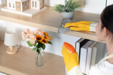 Kendini işine adamış bir kadın parlak bir odada ahşap rafları temizliyor, ev temizliğine ve düzenine bağlılığını gösteriyor..