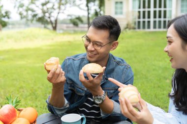 Güneşli bir bahçede gülümseyen ve hamur işi paylaşan genç bir çift, bağlantıyı ve sağlıklı yaşamı vurguluyor..