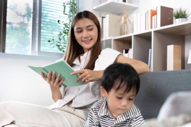 Neşeli bir anne, küçük oğlu oynarken okumakla meşgul. Besleyici bir ev ortamı ve aile bağlarının önemini gösteriyor..