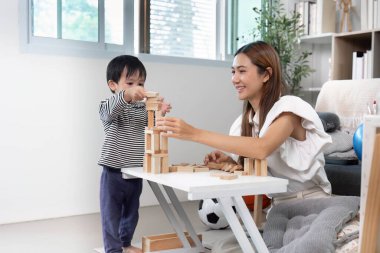 Bir anne ve oğlu, parlak bir oturma odasında yaratıcılığı ve takım çalışmasını teşvik eden ahşap bloklardan bir kule inşa ediyorlar..