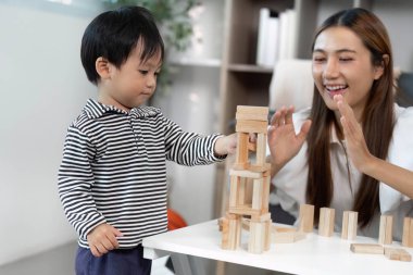 Genç bir çocuk neşeyle ahşap bloklardan bir kule inşa ederken, bakıcı da besleyici bir çevrede oynamaya teşvik ediyor..