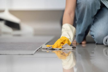 Sarı eldivenli bir kişi bir bez ile yerleri siler, temizliği ve evde bakımı vurgular..