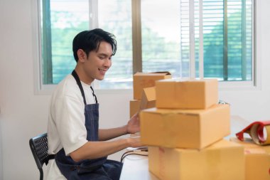 Genç bir girişimci masasında çalışır, paketleri ve lojistiği yönetir, uzak çalışma yaşam tarzı ve verimliliğini ön plana çıkarır..