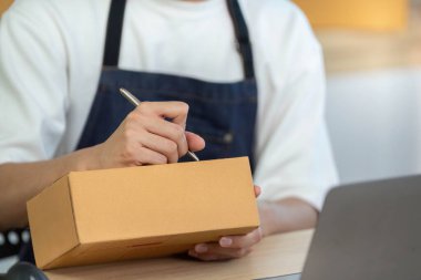 Önlüklü genç bir adam, modern bir ofis masasında otururken teslimat için bir paket imzalar..