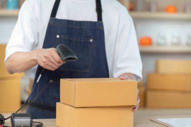 Bir işçi, e-ticaret lojistiğinin altını çizen bir nakliye bölgesinde barkod tarayıcısı olan bir paketi tarıyor..