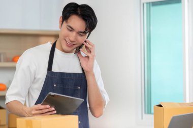 Bir nakliye departmanındaki tableti kontrol eden genç bir işçi e-ticarette birden fazla iş göstererek telefonda konuşuyor..