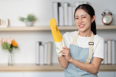 Genç bir kadın lastik eldiven giyerken gülümsüyor, temizlik görevlerini hevesle ve olumlu bir şekilde üstlenmeye hazır..