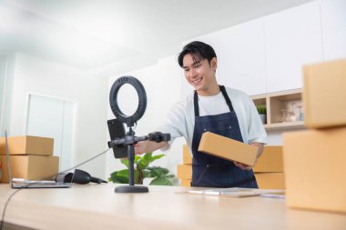 Genç bir adam, nakliye için paketler hazırlarken, e-ticareti canlı yayın ile harmanlarken, seyircileriyle meşgul oluyor..