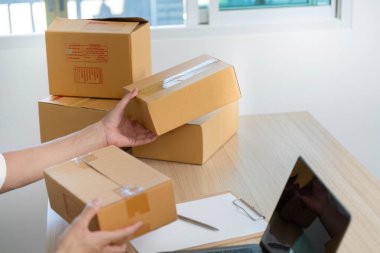 Genç bir adam masasındaki paketleri düzenliyor, iyi aydınlatılmış bir ofis ortamında nakliyeye hazırlanıyor..