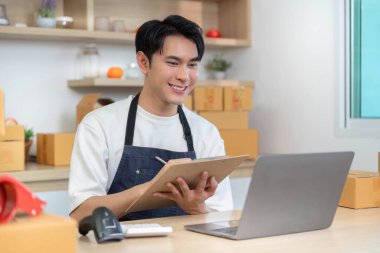 Neşeli bir e-ticaret çalışanı, online sipariş yönetimindeki verimliliği vurgulayarak bir dizüstü bilgisayar kullanırken ayrıntıları bir panoya kaydediyor..