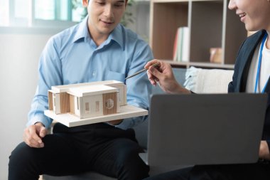 İki mimar, modern bir ofiste tasarım elementlerini ve proje detaylarını tartışarak bir yapı modelini analiz eder..