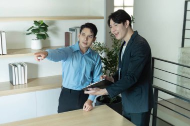 Bir emlakçı müşteriye bir mülkün özelliklerine dikkat çeker. Detayları şık bir ofis ortamında vurgular..