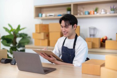 Genç bir adam talimatları incelerken gülümsüyor. Parlak ve düzenli bir çalışma alanında dizüstü bilgisayar kullanıyor..