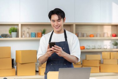 Genç bir işçi, modern e-ticaret uygulamalarını yansıtan bir nakliye departmanında akıllı telefon kullanırken gülümsüyor..