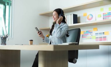 Müzikten hoşlanan ve şık bir ofis ortamında akıllı telefonuyla çalışan bir grafik tasarımcısı..