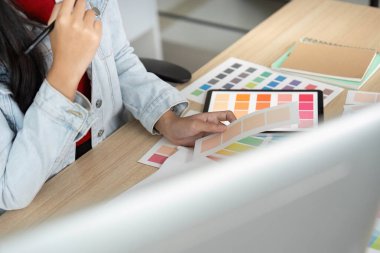 Genç bir kadın masasında otururken tabletindeki renk örneklerini inceliyor, tasarım sürecini ve yaratıcılığını gösteriyor..