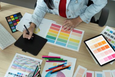 Renk örneklerini analiz eden ve modern bir çalışma alanında tablet üzerinde tasarımlar yapan bir grafik tasarımcısı.