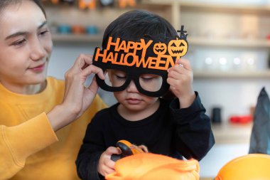 Bir anne oğluna neşeli bir Cadılar Bayramı gözlüğü takması için yardım eder. Tatil hazırlıkları için eğlenceli bir ortam yaratır..