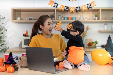 Bir anne ve oğlu, neşeli bir anın tadını çıkarırlar. Cadılar Bayramı ruhunu gösterirler ve şenlikli dekorasyonlarla meşgul olurlar..