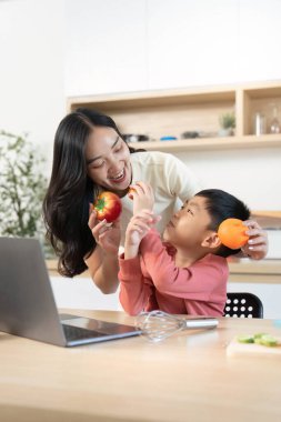 Bir anne ve oğlu, sağlıklı beslenmenin ve aile eğlencesinin önemini vurgulayarak, mutfaktaki meyvelerle neşe içinde etkileşime geçiyorlar..
