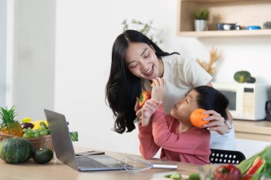 Bir anne ve oğlu, gülerken portakallarını paylaşır. Parlak bir mutfak ortamında sağlıklı atıştırma ve aile bağlarını teşvik ederler..