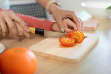 Bir annenin, oğlunun taze domatesleri dilimlemesine ve sağlıklı yemek hazırlama konusunda takım çalışması yapmasına yardımcı olduğu ortak bir yemek anı..