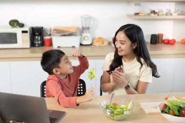 Parlak bir mutfakta sağlıklı beslenme alışkanlıklarını teşvik eden taze bir salata hazırlayan bir anne ve oğlu arasında neşeli bir an..