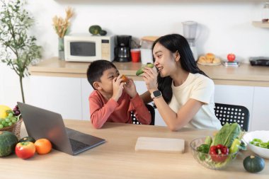 Bir anne ve oğlu sıcacık bir mutfakta sağlıklı atıştırmalıkların keyfini çıkarırlar. Aile bağlarını ve besleyici yeme alışkanlıklarını vurgularlar..
