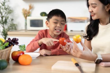 Bir anne ve oğlunun sağlıklı yemek pişirme, modern bir mutfaktan taze domates ve portakal seçme konusunda bağ kurdukları neşeli bir an..