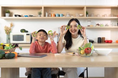 Bir anne ve oğlu, evde sağlıklı yemek pişirmenin yaratıcılığını ve eğlencesini gösteren dolmalık biber şekillerini neşeyle elinde tutuyorlar..