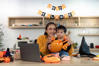 Neşeli bir anne ve oğlu Cadılar Bayramı süsleriyle poz veriyor, balkabakları ve balonlar da dahil, festival sezonunu kutluyorlar..