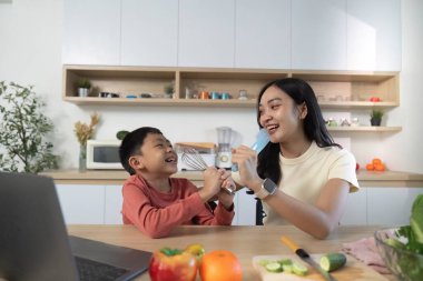 Neşeli bir anne ve oğlu, neşeli bir mutfakta birlikte sağlıklı yemekler hazırlarken, aile bağlarını ve sağlıklı beslenmeyi desteklerken, kahkahalarını paylaşıyorlar..