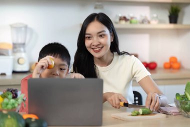 Bir anne ve oğlu, bir dizüstü bilgisayarla sağlıklı bir yemek hazırlarken bir anlık sevinçlerini paylaşıyorlar. Aileye ve beslenmeye odaklan.