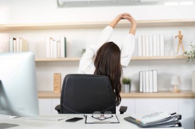 Genç bir kadın, işyerinde ergonominin ve kendine bakmanın önemini vurgulayarak sırtına yaslanıyor..