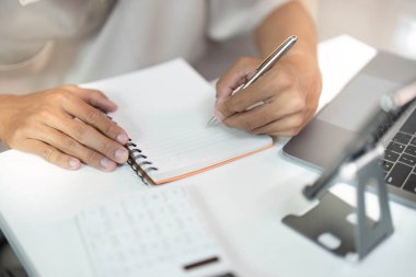 Bir dizüstü bilgisayarla temiz bir masada çalışırken fikirlerini not eden odaklanmış bir insan. Üretkenliği ve organizasyonu temsil eder.