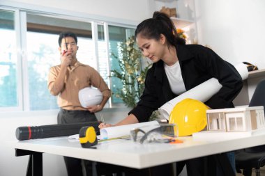Mühendisler, parlak bir ofiste inşaat planları ve modellerini analiz ederek, işbirliği ve yenilikleri vurguladılar..