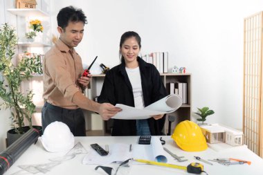 Modern bir çalışma alanında modeller ve planlar inşa etmeyi tartışan iki mimar, takım çalışmasını ve yaratıcılığı ön plana çıkarıyor.