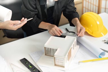 Mühendisler parlak bir ofisteki araçlarla bir yapı modelini ölçüyorlar, hassasiyet ve takım çalışması sergiliyorlar..