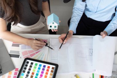 İki mimar sürdürülebilir bir ev tasarımı hakkında yaratıcı bir tartışmaya girişirler, fikirlerini görselleştirmek için bir model ve planlar kullanırlar..