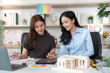 İki kadın mimar bir mimari tasarım projesinde iş birliği yapıyor, renk paletleri ve yaratıcı bir çalışma alanında bir model kullanıyorlar..