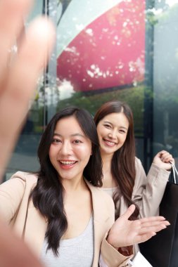 İki arkadaş bir mağazanın önünde özçekim için poz veriyor, alışveriş çantalarını sergiliyorlar ve Kara Cuma anlaşmaları için heyecanlanıyorlar..